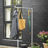 Portant à vêtements argenté sur pieds placé sur une terrasse pour suspendre sac à main et parapluie à l'aide de crochet en forme de S